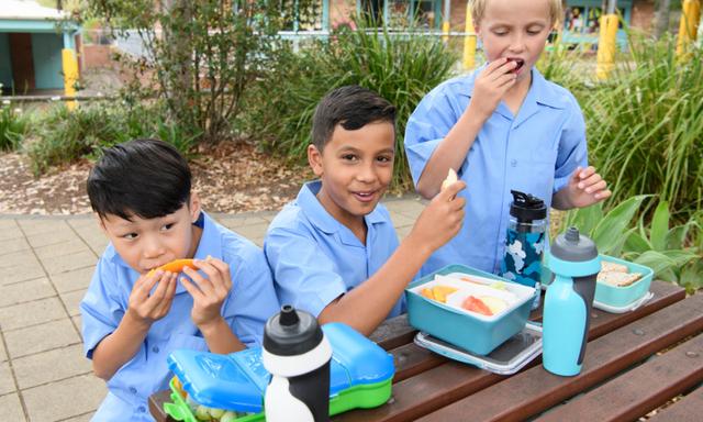 Multi racial school boys sitting at table outdoors and eating food on school lunch break