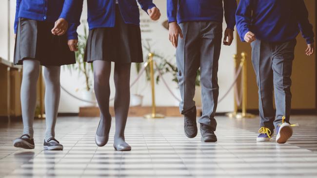 Cropped image of school kids in uniform walking together in a row through corridor. Focus on legs of students walking through school hallway.