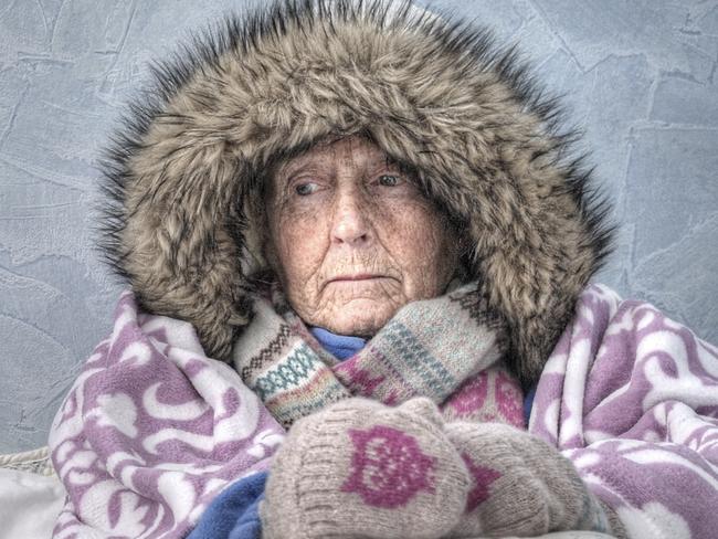 Senior couple, too cold to get out of bed, miserable, in inadequate housing, unable to afford heating. They are wrapped in blankets, wearing hats, scarves, gloves and winter coats.