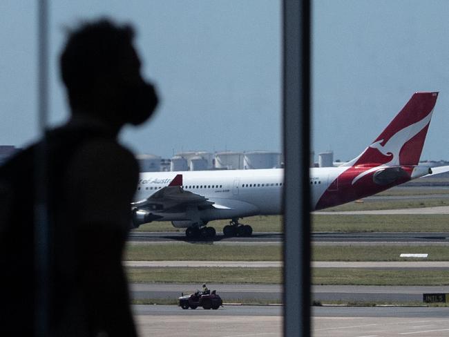 SYDNEY, AUSTRALIA - NewsWire Photos December 9, 2020: Qantas aircraft seen on the runway as a passenger passes through the terminal in the foreground at Sydney International Airport. Picture: NCA NewsWire / James Gourley