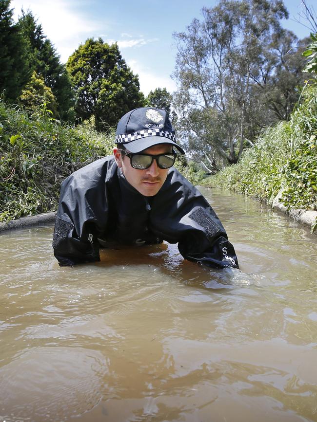 A police officer combs Dandenong Creek for evidence linked to Paul Virgona’s death. Picture: David Caird