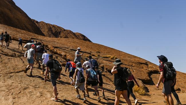 Tourists are seen climbing Uluru, ignoring the sign from the Traditional Owners. Picture: AAP Image/Lukas Coch.