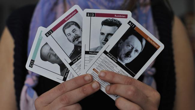 A woman holds up cards featuring (from L to R) Mao Zedong, Josef Stalin, Nicolae Ceausescu and Adolf Hitler.