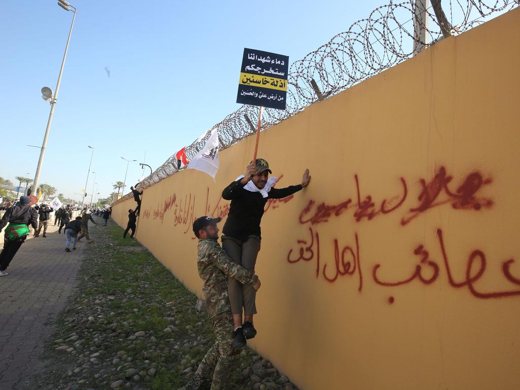 A member of an Iraqi Shiite paramilitary group helps a fellow protesters holding a placard denouncing the United States climb on the outer wall of the US embassy in Baghdad's Green Zone during an angry demonstration. Picture: AFP