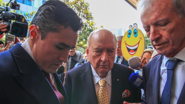 Danny Lim’s emoji placard is visible behind Alan Jones as he arrived at Sydney’s Downing Centre Local Court to face allegations of sexual assault on Wednesday. Picture: Roni Bintang/Getty Images