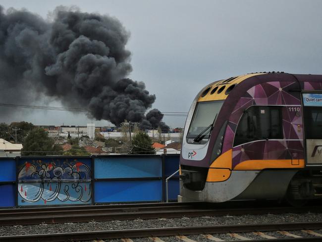 A V/Line train heads city bound as a large factory fire burns out of control in West Footscray. Picture: Mark Stewart