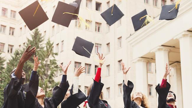 A group of multietnic students celebrating their graduation by throwing caps in the air. Education, qualification and gown concept.