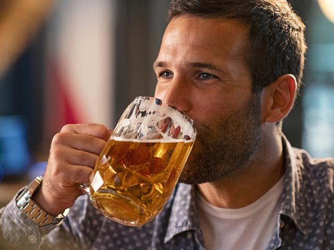 Handsome young man drinking a pint of beer while looking away. Cheerful mid man in casual clothing feeling relaxed while enjoying draft beer in bar. Middle aged guy take a sip from his drink at pub during the night.