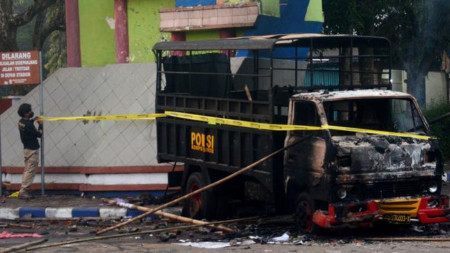 A policeman sets up a cordon next to a torched vehicle outside Kanjuruhan stadium in Malang on Sunday. Picture: AFP