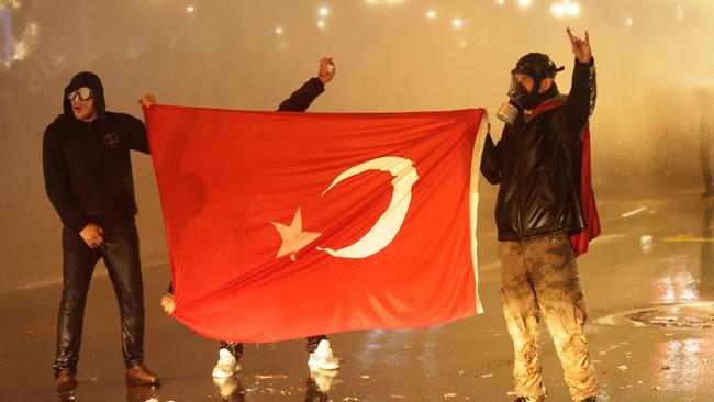 TOPSHOT - Protesters hold a Turkish national flag as they clash with Turkish anti riot police using tear gas and water cannons during a demonstration in support of Istanbul's arrested mayor, in Ankara on March 23, 2025. Istanbul's newly-deposed mayor Ekrem Imamoglu was taken to a jail on the western outskirts of the megacity city on March 23, 2025 afternoon, the main CHP opposition party said. (Photo by Adem ALTAN / AFP)