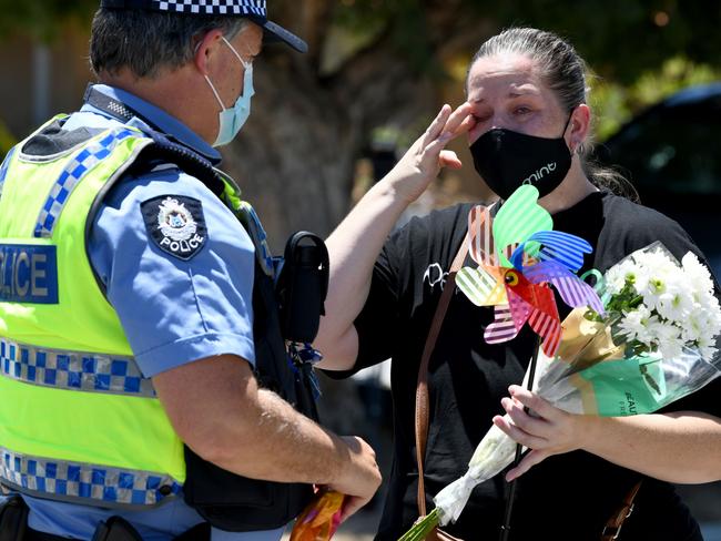 A distraught woman brings flowers and a colourful windmill to a police officer at the scene. Picture: NCA NewsWire / Sharon Smith