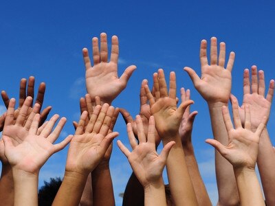 multi-ethnic volunteer group raising hands against blue sky