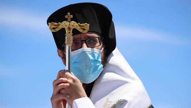 Bishop Silouan got a day pass to leave quarantine to give his blessing wearing a mask on the Glenelg Jetty for the Blessing of the Waters religious ceremony. Picture: Russell Millard