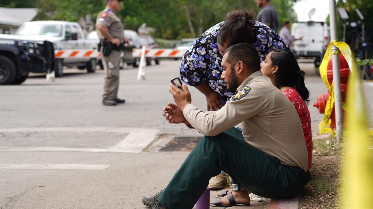 A sheriff checks his phone as he sits on the sidewalk with two women outside Robb Elementary School as state troopers monitor the area. Picture: Allison Dinner/AFP