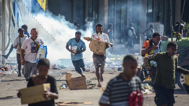 Crowds leave shops with looted goods in Port Moresby. Picture: AFP