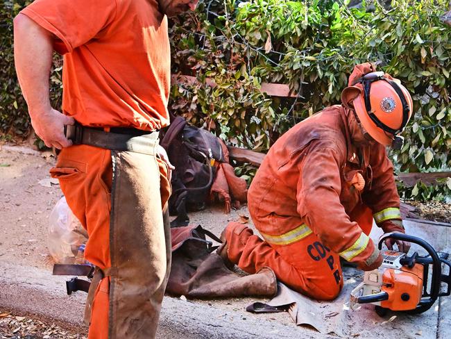 Inmate firefighters in their orange firefighting gear gather equipment beside a Cal Fire firetruck in the Mandeville Canyon neighborhood of Los Angeles, California. Picture: AFP