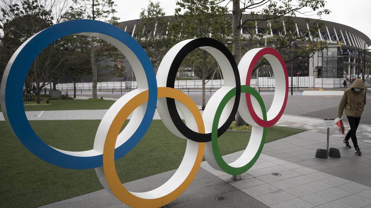 A man wearing a face mask walks past the Olympic rings in front of the National Stadium, the main arena for the postponed Tokyo 2020 Olympic and Paralympic Games. Picture: Getty Images