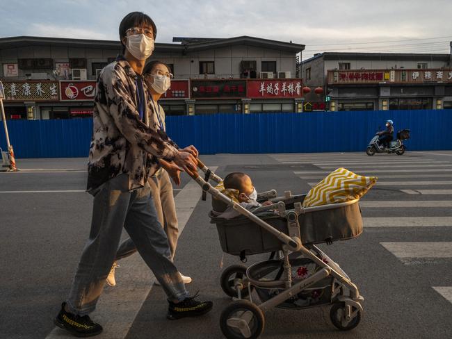 BEIJING, CHINA - MAY 18: A couple push a stroller as they walk by a neighbourhood fenced-in and under lockdown after recent COVID-19 outbreaks in the area on May 18, 2022 in Beijing, China. China is trying to contain a spike in coronavirus cases in the capital Beijing after hundreds of people tested positive for the virus in recent weeks, causing local authorities to initiate mass testing, mandate proof of a negative PCR test within 48 hours to enter many public spaces, to close schools and retail stores, ban gatherings and inside dining in all restaurants, and to lockdown many neighbourhoods in an effort to maintain the country's zero COVID strategy. (Photo by Kevin Frayer/Getty Images)