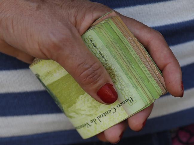 FILE - In this Feb. 7, 2018 file photo, a woman holds a wad of bills to pay her bus fare in Caracas, Venezuela. The IMF predicted on Monday, July 23, 2018 that inflation in Venezuela would reach one million percent this year, comparable to that experienced in Germany at the beginning of the 20th century and in Zimbabwe at the beginning of the last decade. (AP Photo/Ariana Cubillos, File)