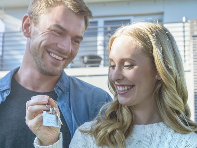 Young couple holding their new house key. They are standing in front of the home in casual clothes. Both are happy, relaxed and smiling. He has a beard and she is blonde. They could be buying or selling real estate. istock