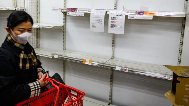 A woman wearing a face mask walks past empty supermarket shelves, usually stocked with toilet paper, in Tokyo, as coronavirus fears set in. Picture: AFP