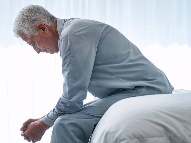 Shot of a depressed senior man sitting on his bed at home