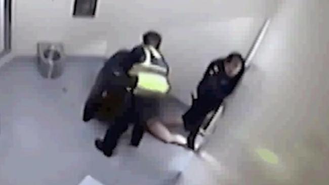 The woman is seen naked from the waist down and an officer stands on her legs.