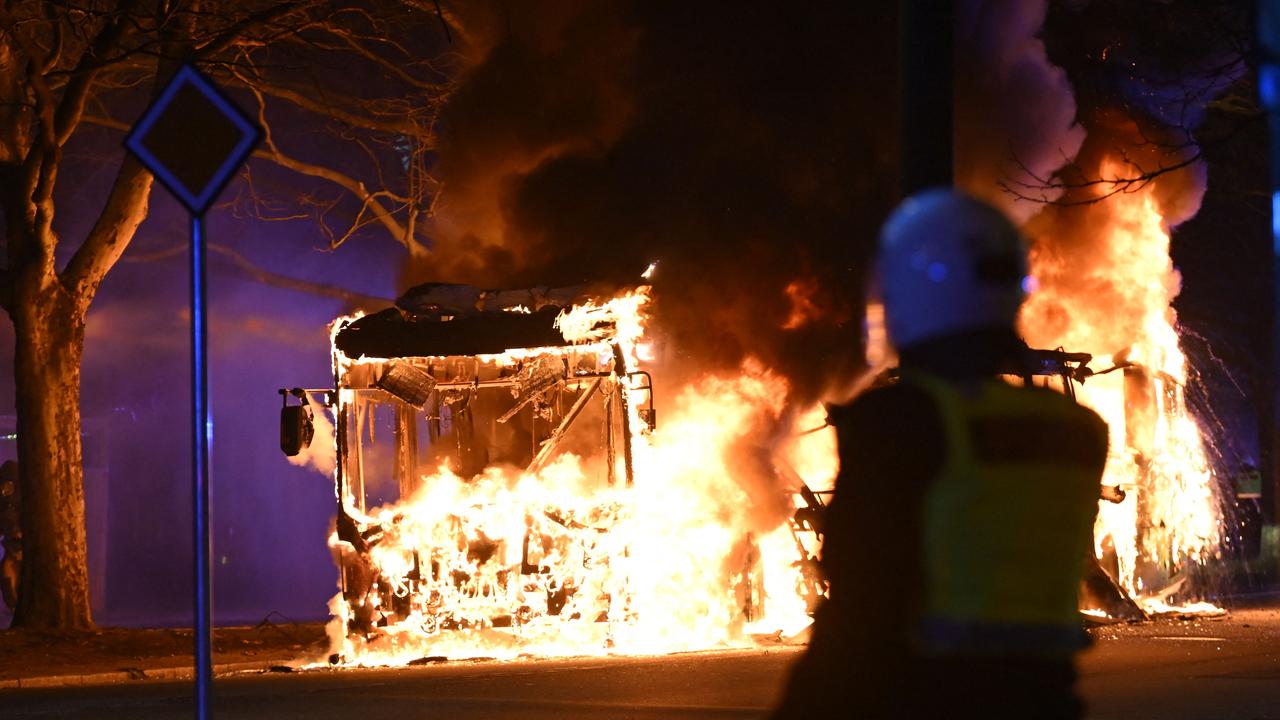 An anti-riot police officer stands next to a city bus burning in Malmo. Photo by Johan NILSSON / TT NEWS AGENCY / AFP)