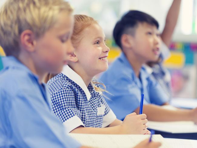 Group of children listening to the teacher. They are in a classroom. Multiethnic group with Caucasian and Asian kids. School girl is smiling and happy