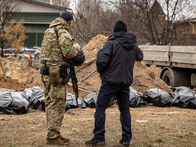 EDITORS NOTE: Graphic content / A member of the Ukrainian army and a policeman stand near body bags exhumed from a mass grave where civilians where buried in Bucha, on the outskirts of Kyiv, on April 13, 2022, amid Russia's military invasion launched on Ukraine. - A visit by the International Criminal Court's chief prosecutor to Bucha -- the Kyiv suburb now synonymous with scores of atrocities against civilians discovered in areas abandoned by Russian forces -- came as the new front of the war shifts eastward, with new allegations of crimes inflicted on locals. (Photo by FADEL SENNA / AFP)