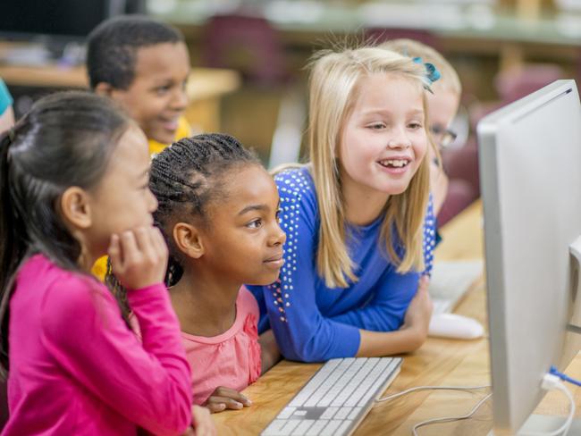 A multi-ethnic group of elementary age children are sitting in the computer lab and are using the computers to play a game together.