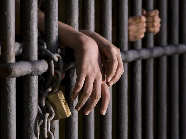 Close up of hands, behind the bars of a prison. Istock