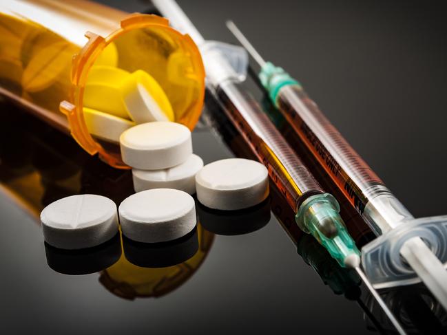 Opioid epidemic, drug abuse concept with closeup on two heroin syringes or other narcotics surrounded by scattered prescription opioids. Oxycodone is the generic name for a range of opioid painkillers