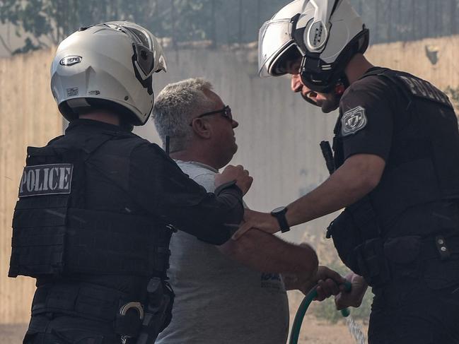 Police officers talk to a man using a hose as they try to evacuate people in the Lagonisi area of Greece amid an ongoing wildfire threat. Picture: Spyros Bakalis / AFP