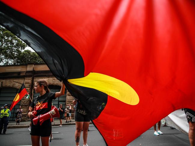 SYDNEY, AUSTRALIA - JANUARY 26: Demonstrators hold up an Aboriginal flag during an Invasion Day protest on January 26, 2024 in Sydney, Australia. Australia Day, formerly known as Foundation Day, is the official national day of Australia and is celebrated annually on January 26 to commemorate the arrival of the First Fleet to Sydney in 1788. Many indigenous Australians refer to the day as 'Invasion Day' and there is a growing movement to change the date to one which can be celebrated by all Australians. In 2024, supermarket Chains Woolworths and Aldi announced that they would stop stocking themed merchandise for the day, drawing a political backlash from opposition leader Peter Dutton. (Photo by Roni Bintang/Getty Images)