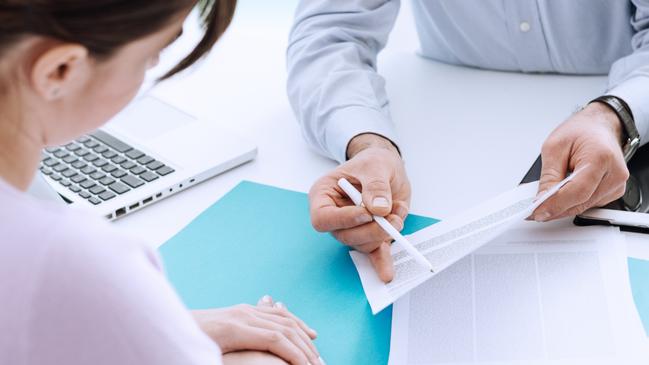 CAREERS: Young woman meeting a professional consultant in his office, he is holding a document and giving explanations.