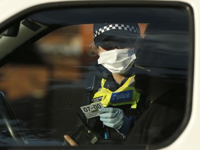 A police officer checks the identification of members of the public at a pop up road block in Broadmeadows. Picture: Getty Images.