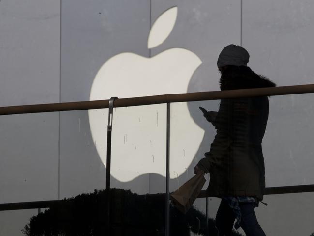 FILE - In this Dec. 23, 2013, file photo, a woman using a phone walks past Apple's logo near its retail outlet in Beijing. Even while it fiercely opposes the FBI’s demand for help unlocking an encrypted iPhone used in the San Bernardino mass shootings, Apple has never argued that it isn’t capable of doing what the government wants. While the FBI may have found an alternative solution in the San Bernardino case, experts say it’s almost certain that Apple and other tech companies will keep increasing the security of their products, making it harder or perhaps even impossible for them to answer government demands for customers’ data. (AP Photo/Ng Han Guan, File)