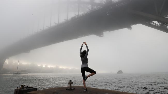 Sandra Peter in front of the Sydney Harbour Bridge in heavy fog this morning in Sydney. Picture: NCA NewsWire / Dylan Coker