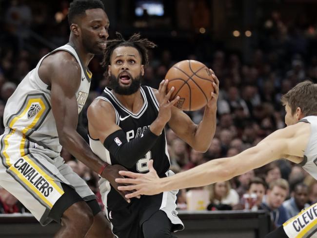 San Antonio Spurs' Patty Mills, center, from Australia, drives between Cleveland Cavaliers' Jeff Green, left, and Kyle Korver in the first half of an NBA basketball game, Sunday, Feb. 25, 2018, in Cleveland. (AP Photo/Tony Dejak)