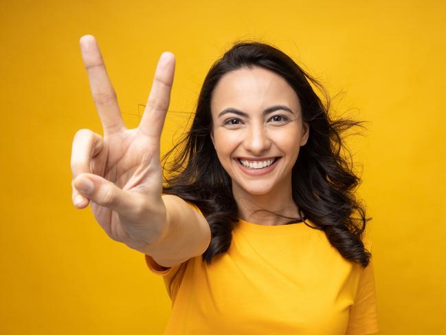 Portrait of young woman wear trendy smart casual outfit isolated on yellow background; two fingers double-digit victory sign generic