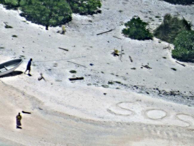 In this Aug. 25, 2016, photo provided by the U.S. Navy, a pair of stranded mariners signal for help as a U.S. Navy P-8A Poseidon aircraft crew from Patrol Squadron (VP) 8 flies over in support of a Coast Guard search and rescue mission on an uninhabited island in Micronesia, Hawaii. The U.S. Coast Guard says the two stranded mariners were rescued Friday after crews saw their "SOS" in the sand. (U.S. Navy via AP)