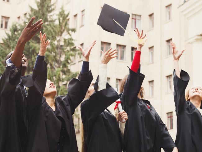 A group of multietnic students celebrating their graduation by throwing caps in the air. Education, qualification and gown concept.