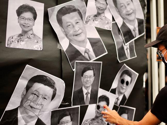 An activist sprays paint on portraits depicting China's President Xi Jinping, Hong Kong's Chief Executive Carrie Lam and Hong Kong's Chief Executive-elect John Lee during a rally to mark the third anniversary of the start of massive pro-democracy protests which roiled Hong Kong in 2019.