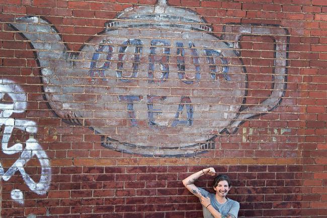 Ghost Signs of Melbourne author Sean Reynolds shows off his Robur Tea tattoo under the sign that inspired it.