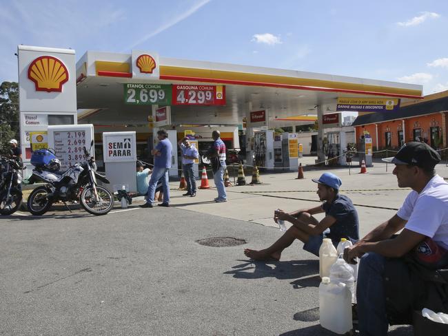 People sit with their containers as they wait at a gas station that is expecting a delivery to refuel, in Sao Paulo, Brazil. Picture: Andre Penner