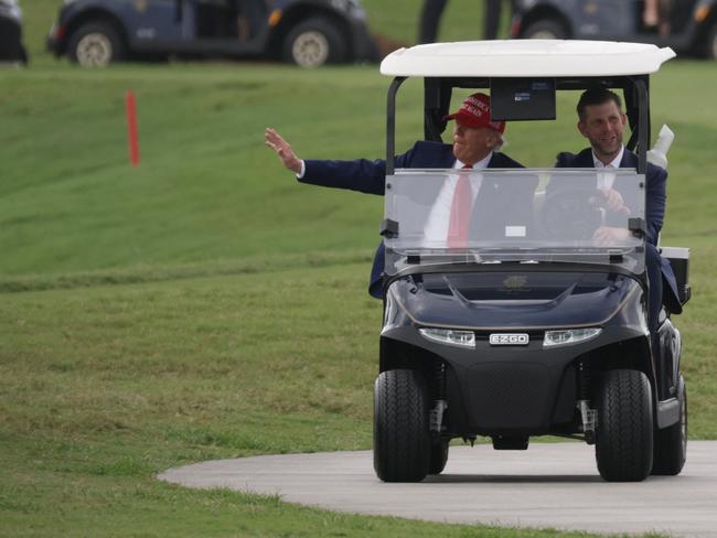 President Donald Trump and his son, Eric Trump, drive in a golf cart on the course where the shooting occurred. Picture: AFP
