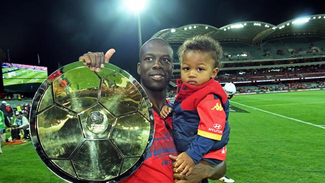Bruce Djite celebrates the victory with son Elijah ... and the trophy after the Reds’ A-League triumph. Picture: Tom Huntley