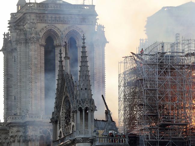 Firefighters tackle the blaze as flames and smoke rise from Notre Dame cathedral as it burns in Paris, Monday, April 15, 2019. Massive plumes of yellow brown smoke is filling the air above Notre Dame Cathedral and ash is falling on tourists and others around the island that marks the center of Paris. (AP Photo/Thibault Camus)