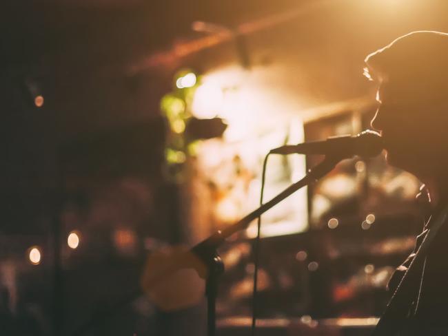 A male singer on a stage performing with guitar at a bar generic, music, microphone, shadow. Picture: iStock